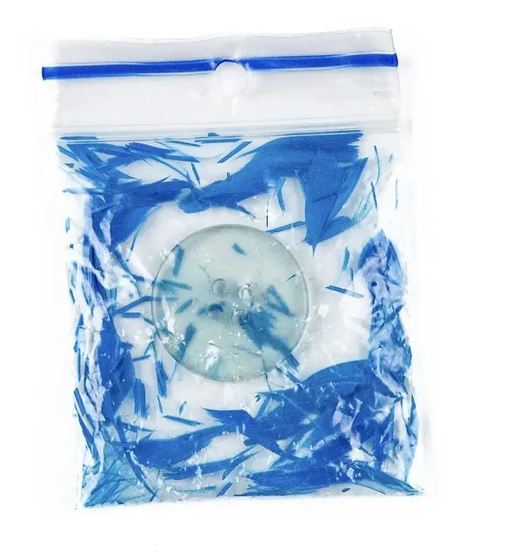 A zip bag filled with shredded blue feathers around a glass disc