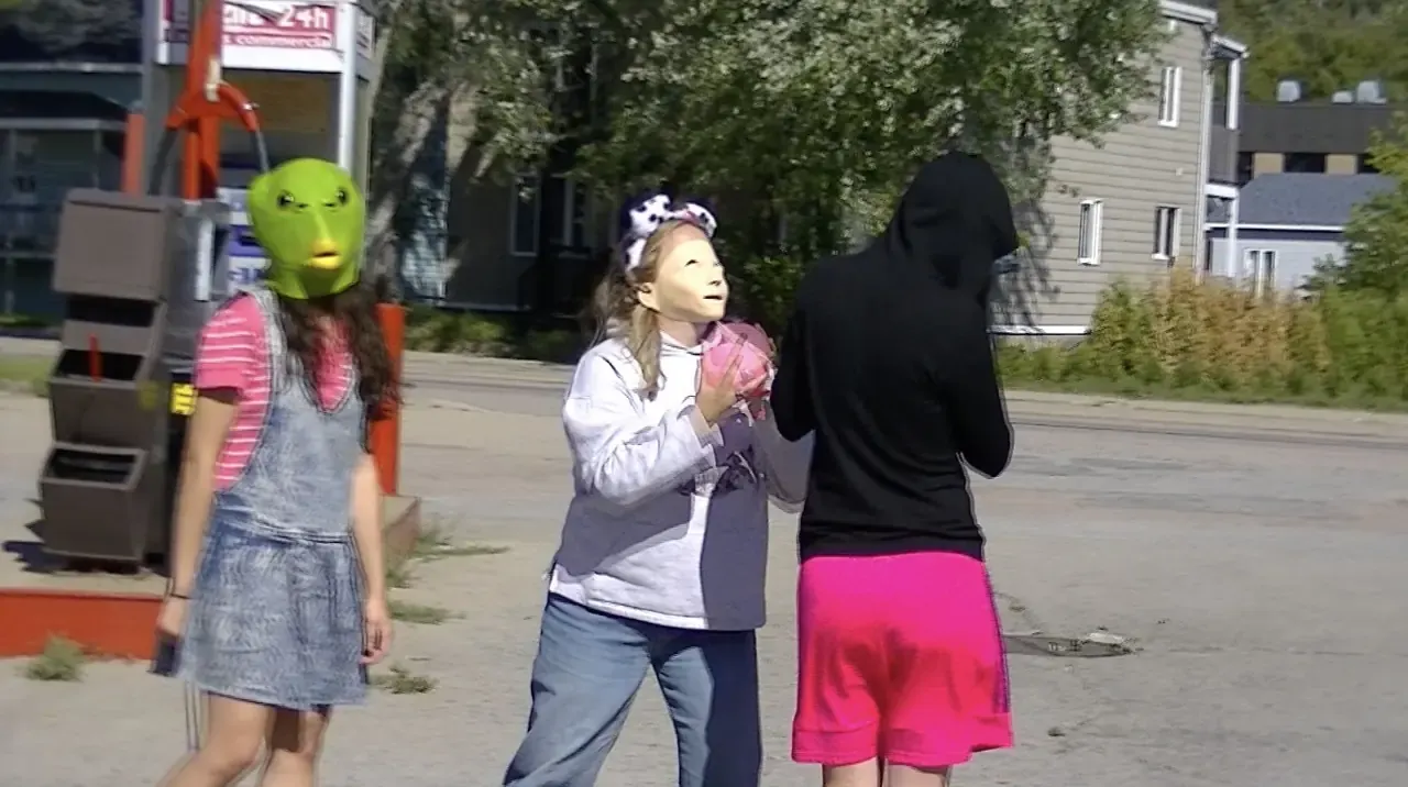 Three kids wearing masks on a street, a still from a video