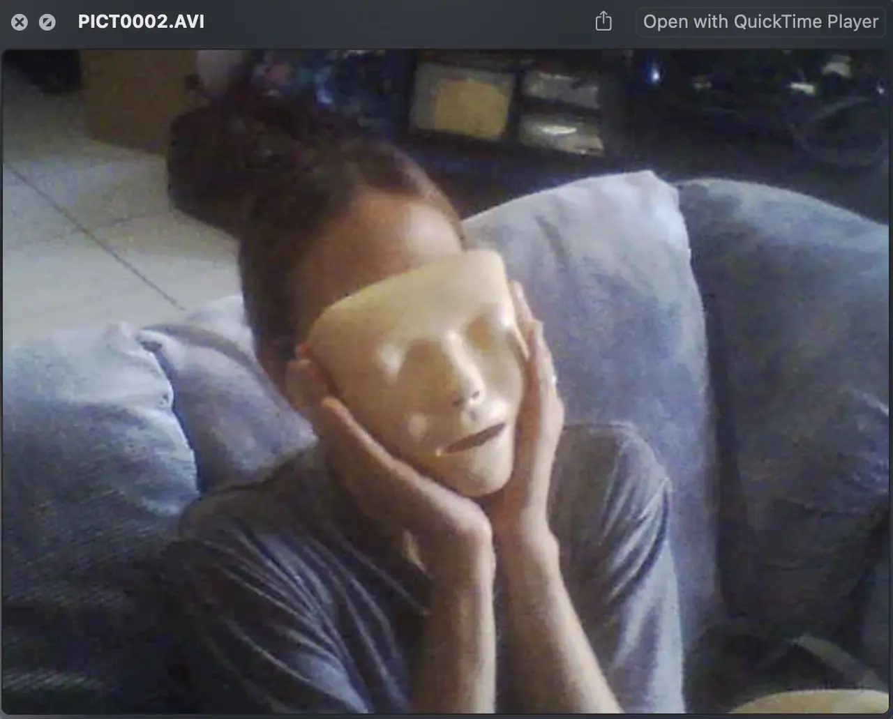 Someone on a couch holding a mask over their face, a still from a home video